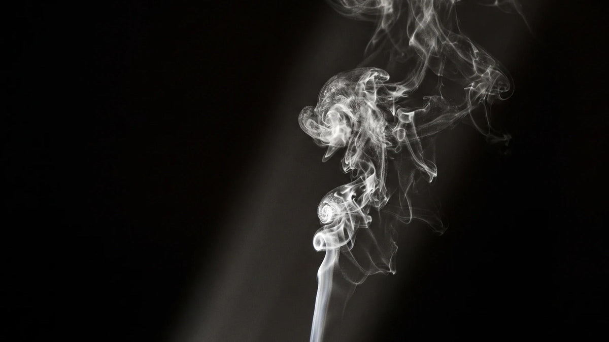A thin plume of white vapour curling and dispersing in a shaft of light against darkness