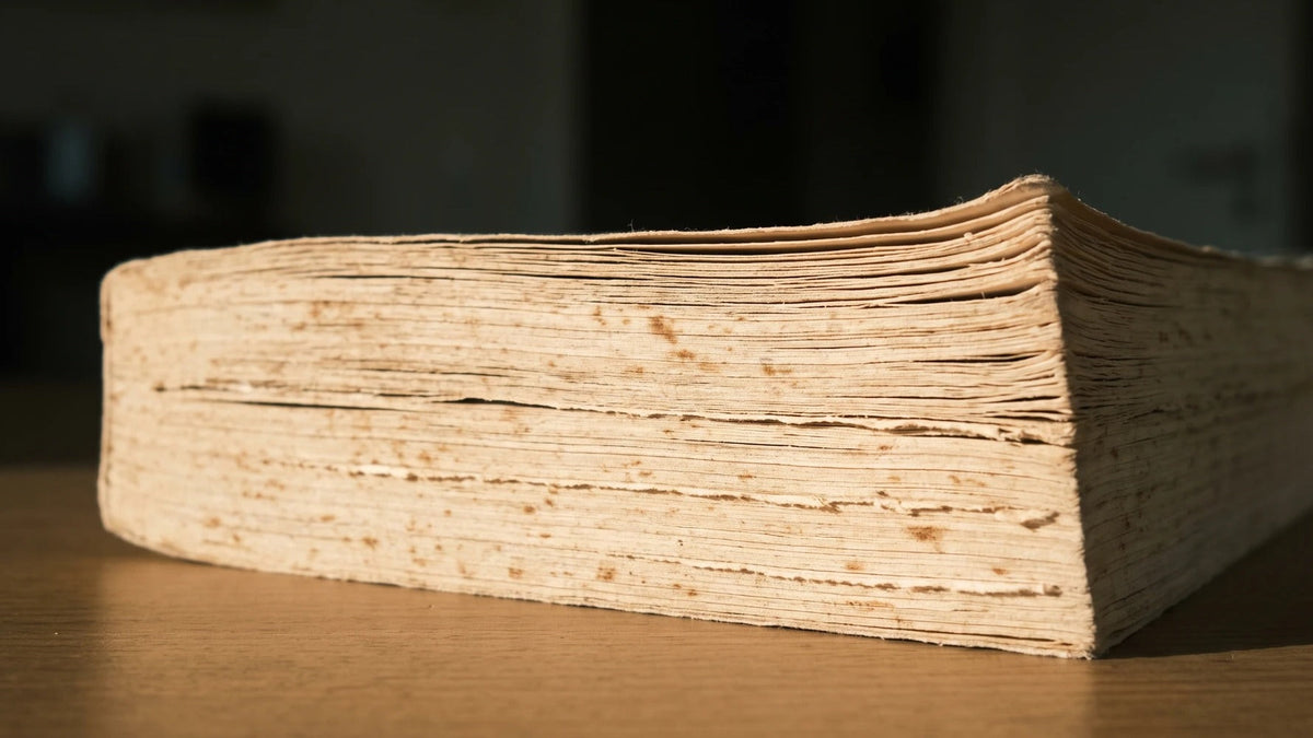 The fanned, foxed page edges of a thick well-used book resting on a wooden table